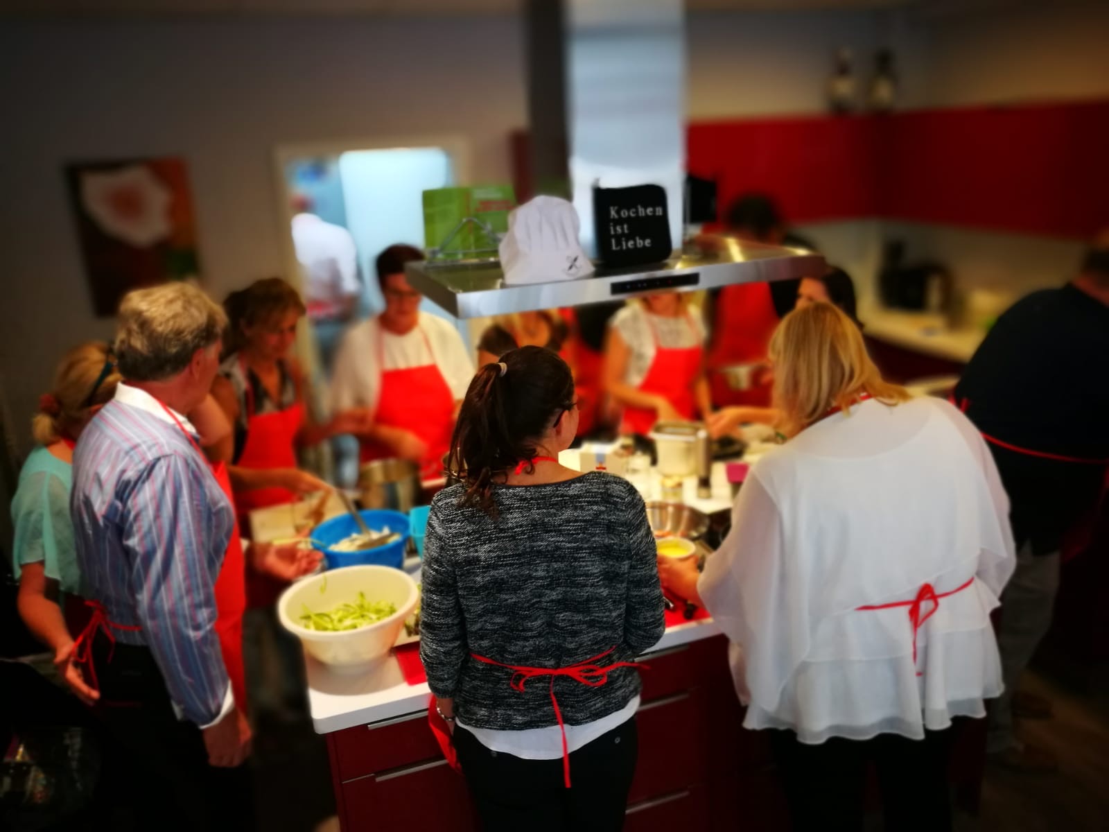 Ein Team in roten Schürzen beim Kochen in der Kochschule