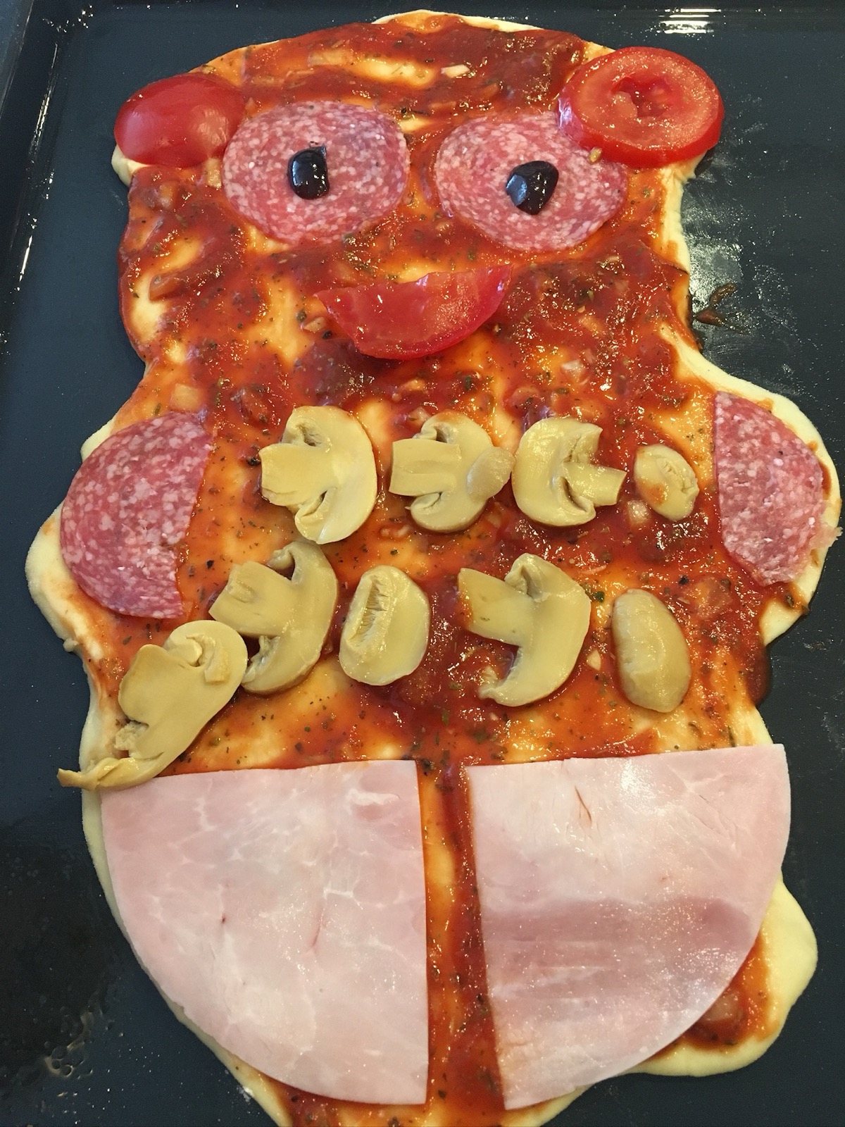 Pizza mit Gesicht aus Salami, Champignons und Tomaten